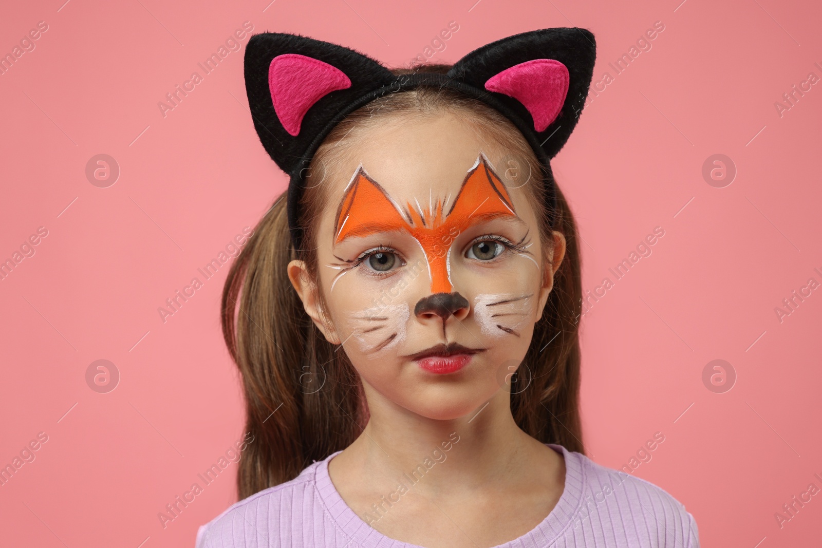 Photo of Cute girl with painted face and ears as cat on pink background