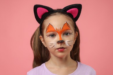 Photo of Cute girl with painted face and ears as cat on pink background