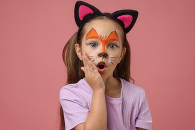 Cute girl with painted face and ears as cat on pink background