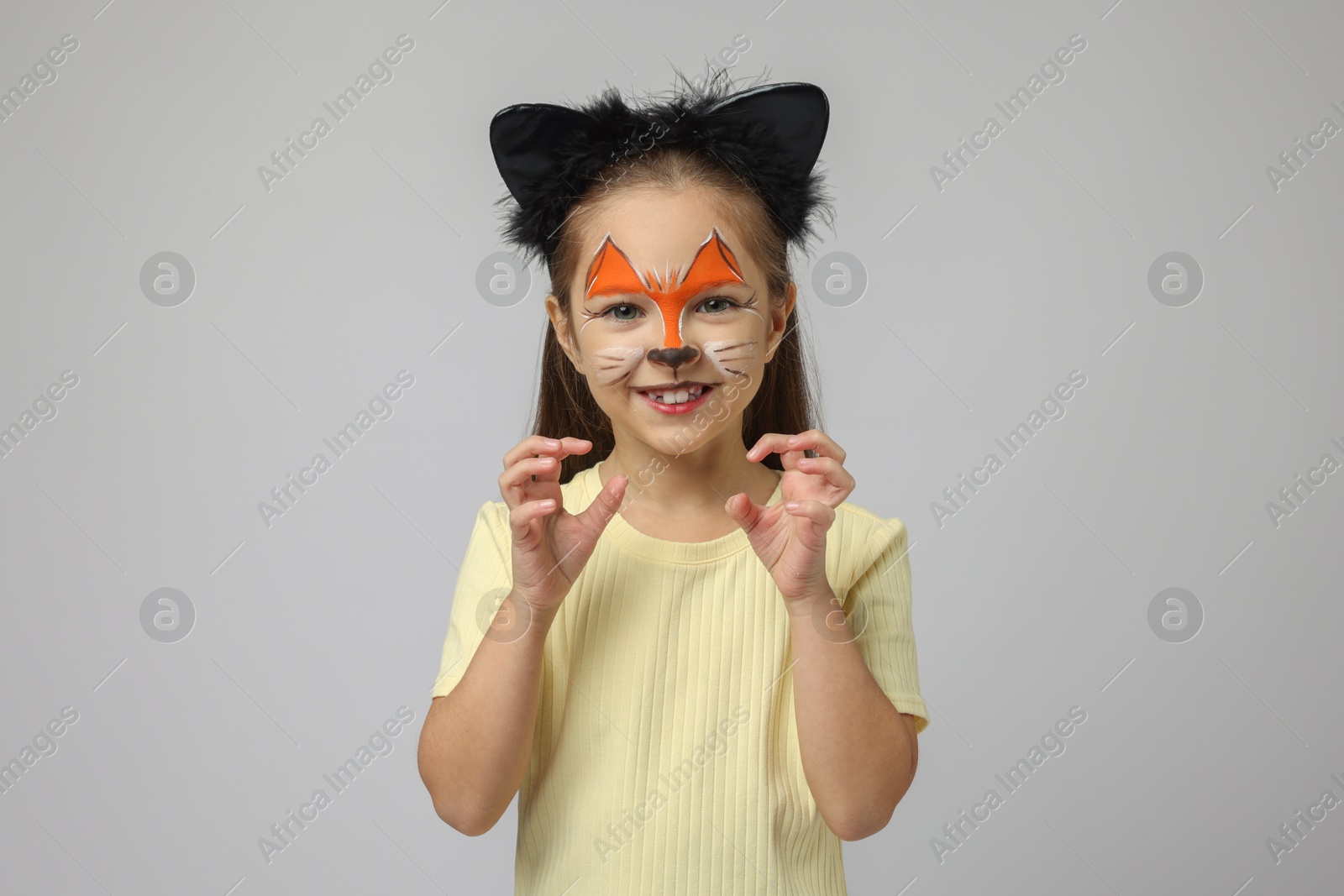 Photo of Cute girl with painted face and ears as cat on grey background