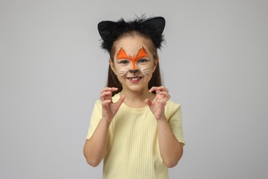 Cute girl with painted face and ears as cat on grey background