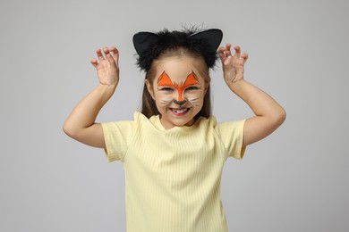 Photo of Cute girl with painted face and ears as cat on grey background