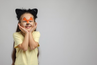 Cute girl with painted face and ears as cat on grey background, space for text