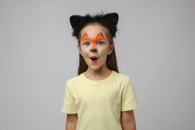 Cute girl with painted face and ears as cat on grey background