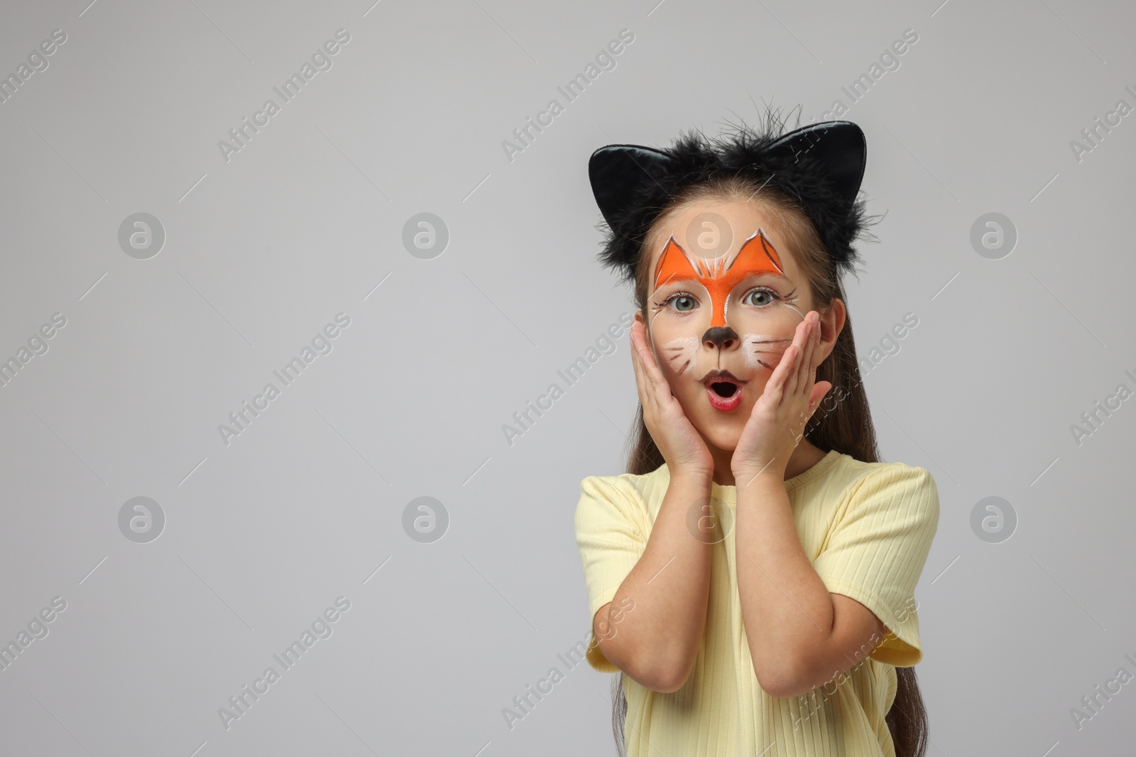 Photo of Cute girl with painted face and ears as cat on grey background, space for text