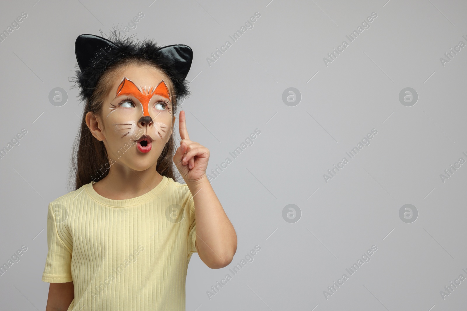 Photo of Cute girl with painted face and ears as cat on grey background, space for text