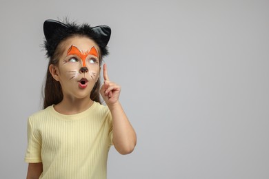 Photo of Cute girl with painted face and ears as cat on grey background, space for text