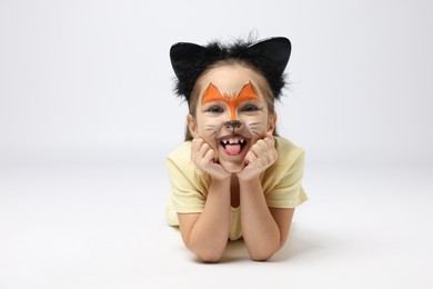 Photo of Cute girl with painted face and ears as cat on grey background