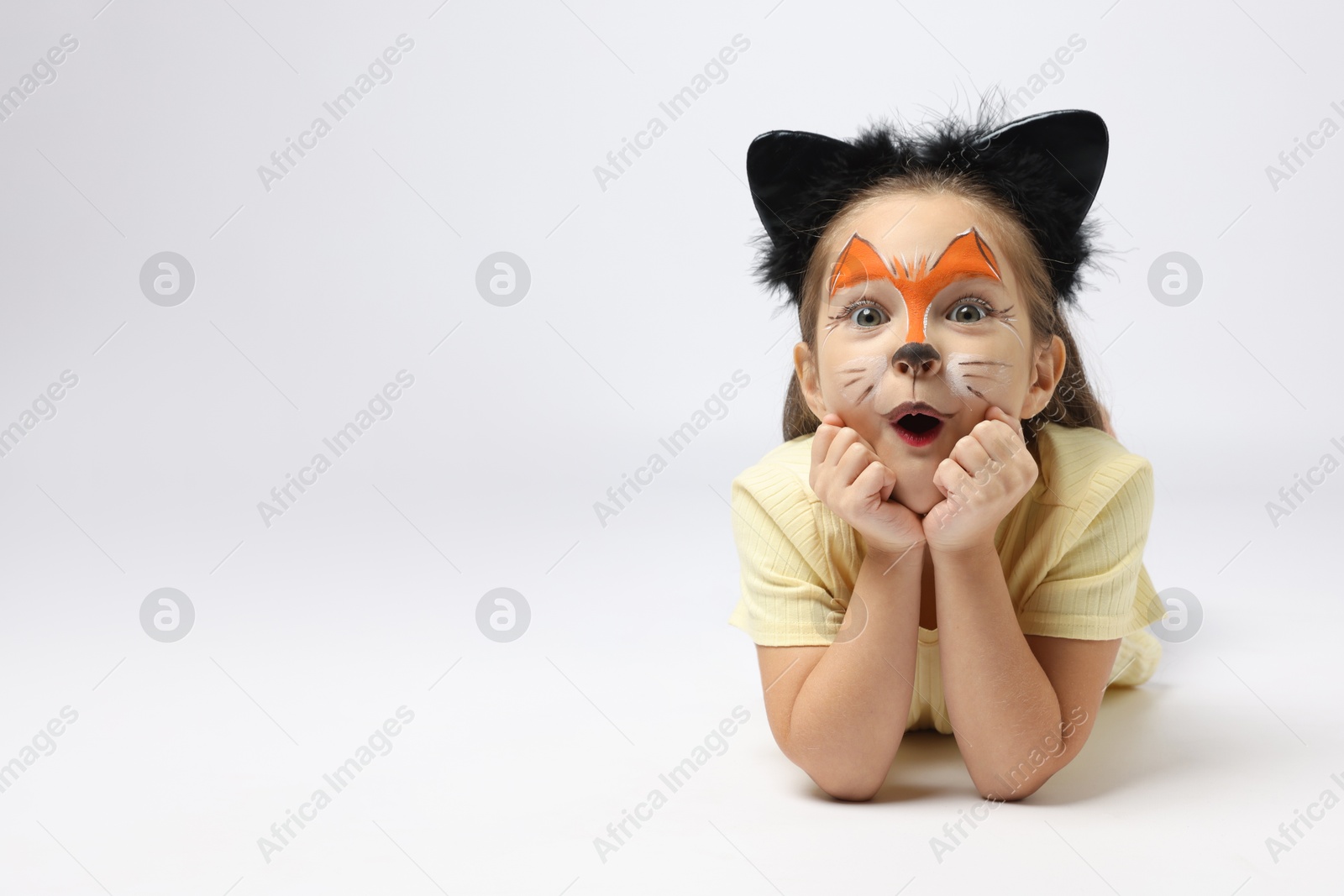 Photo of Cute girl with painted face and ears as cat on grey background, space for text