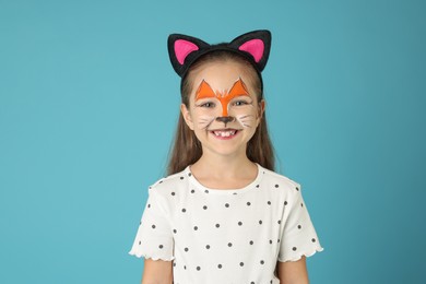 Photo of Cute girl with painted face and ears as cat on light blue background