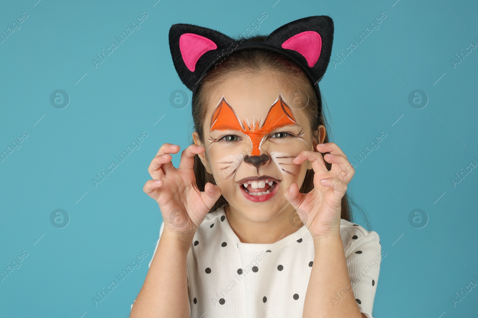 Photo of Cute girl with painted face and ears as cat on light blue background