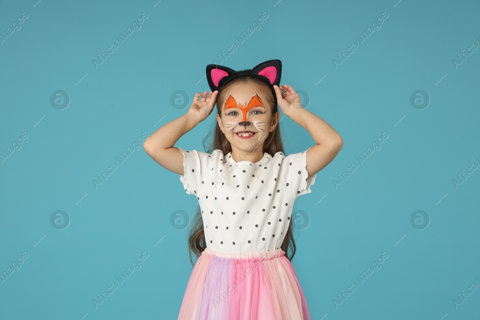 Photo of Cute girl with painted face and ears as cat on light blue background