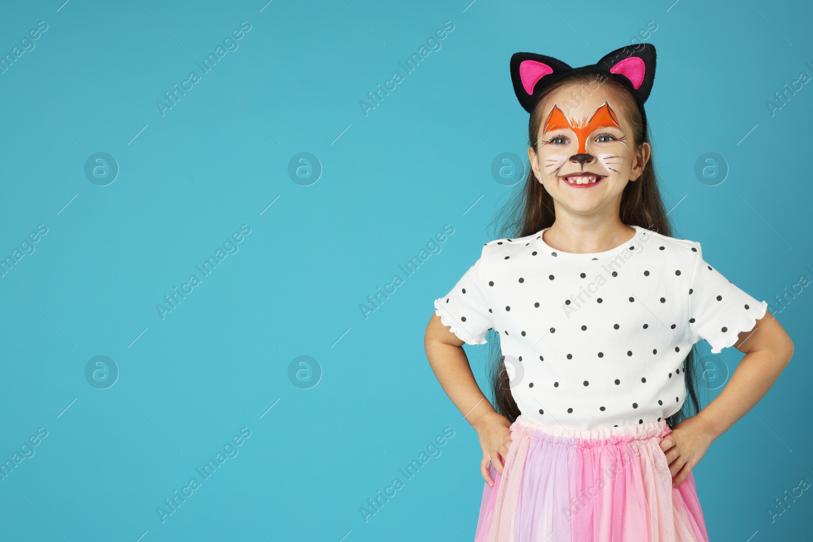 Photo of Cute girl with painted face and ears as cat on light blue background, space for text