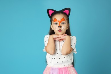 Cute girl with painted face and ears as cat on light blue background, space for text