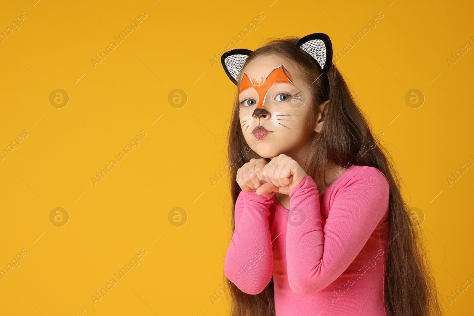 Photo of Cute girl with painted face and ears as cat on orange background, space for text