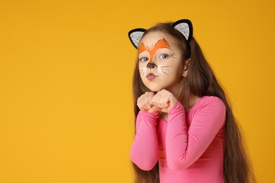 Cute girl with painted face and ears as cat on orange background, space for text