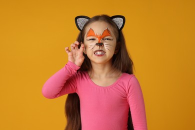 Cute girl with painted face and ears as cat on orange background