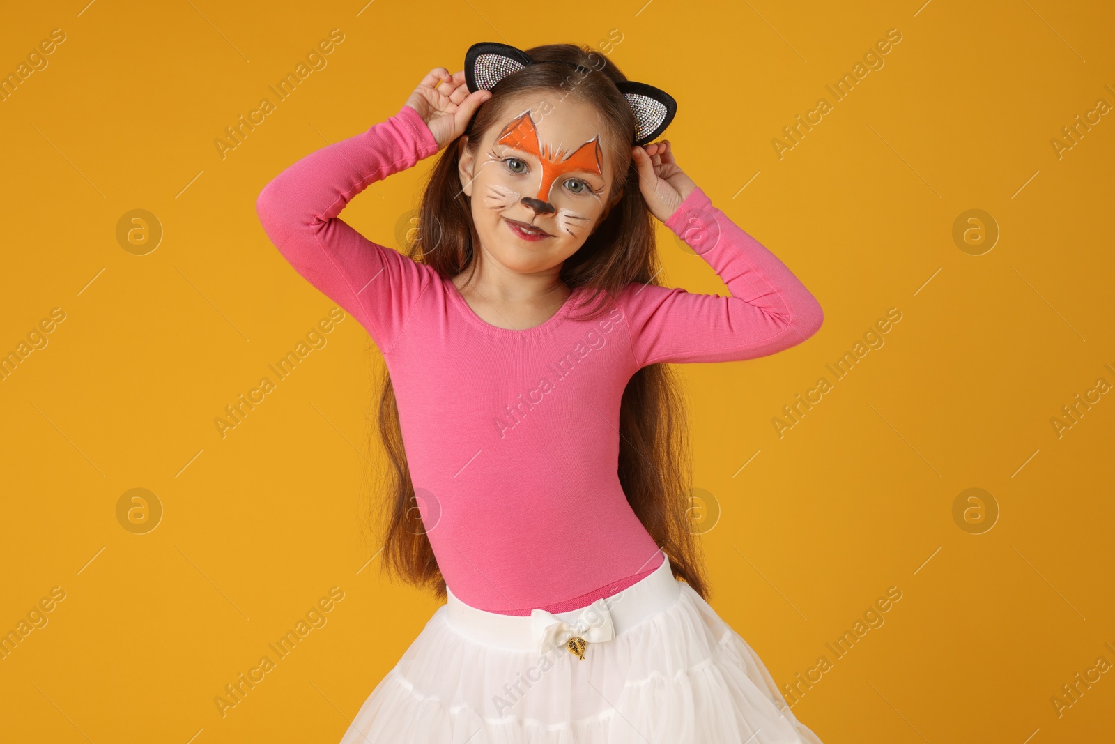 Photo of Cute girl with painted face and ears as cat on orange background