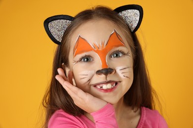 Cute girl with painted face and ears as cat on orange background