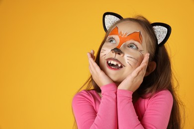 Cute girl with painted face and ears as cat on orange background, space for text