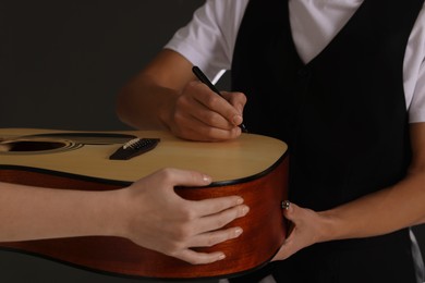 Photo of Musician signing autograph on guitar against black background, closeup