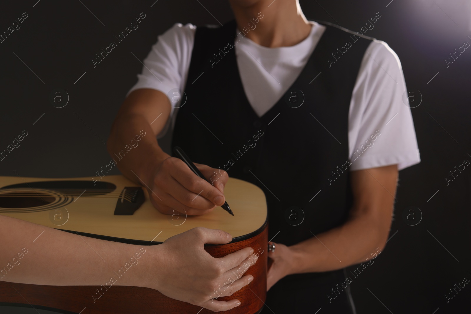 Photo of Musician signing autograph on guitar against dark background, closeup