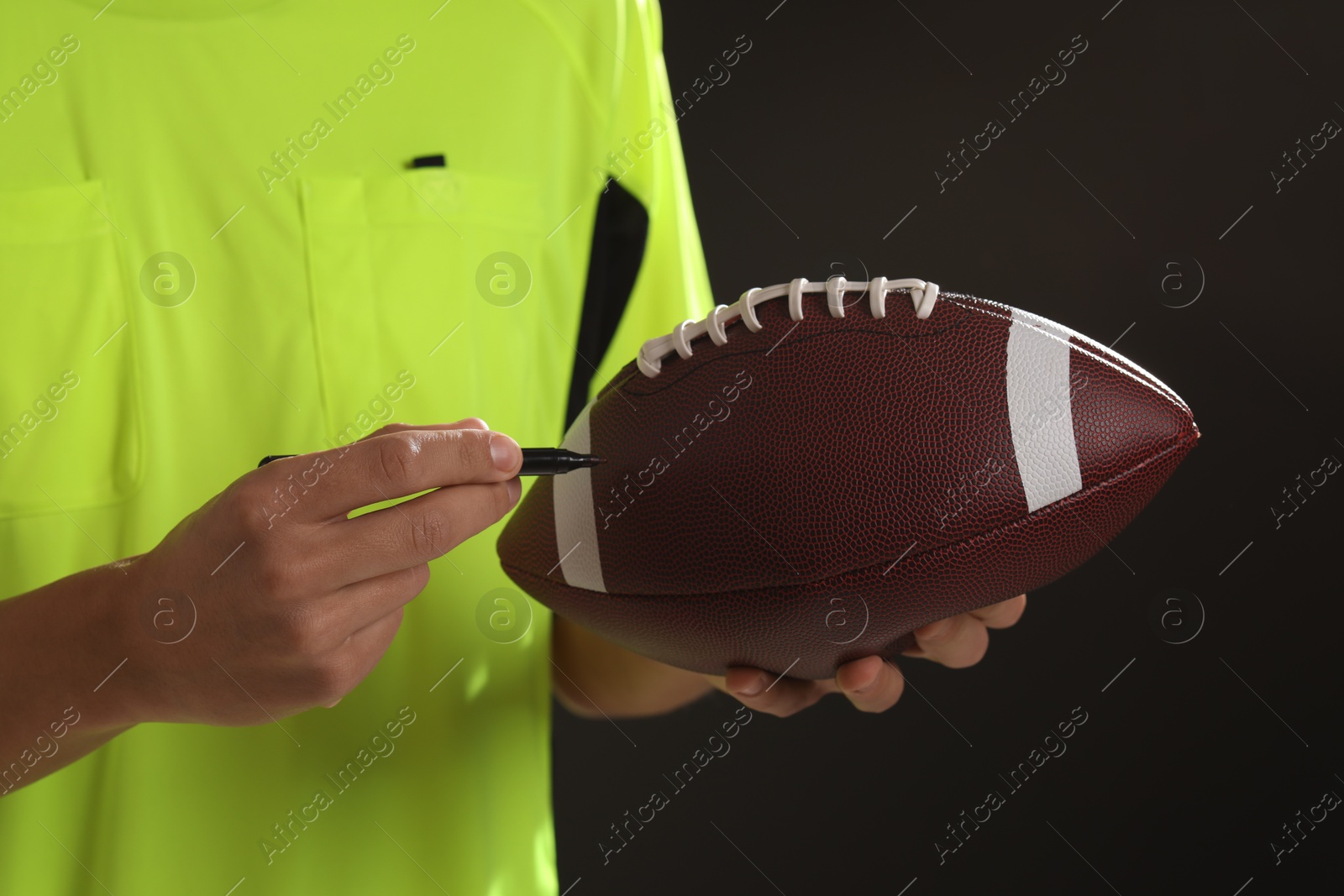 Photo of Professional player signing autograph on American football ball black background, closeup