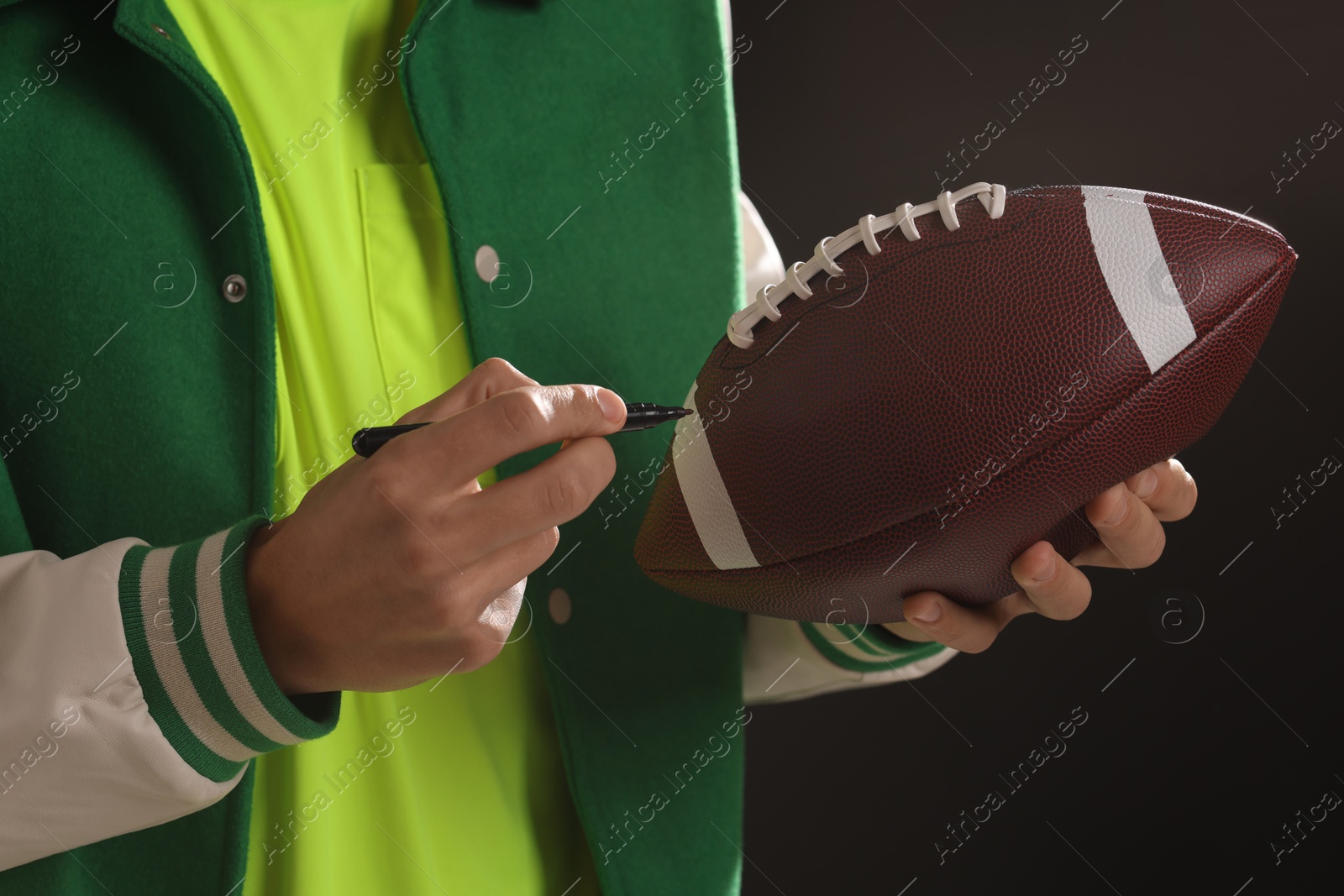 Photo of Professional player signing autograph on American football ball black background, closeup