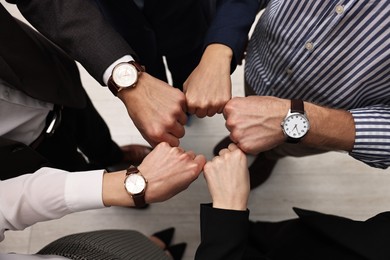 Photo of Teamwork. Group of people joining fists together indoors, top view