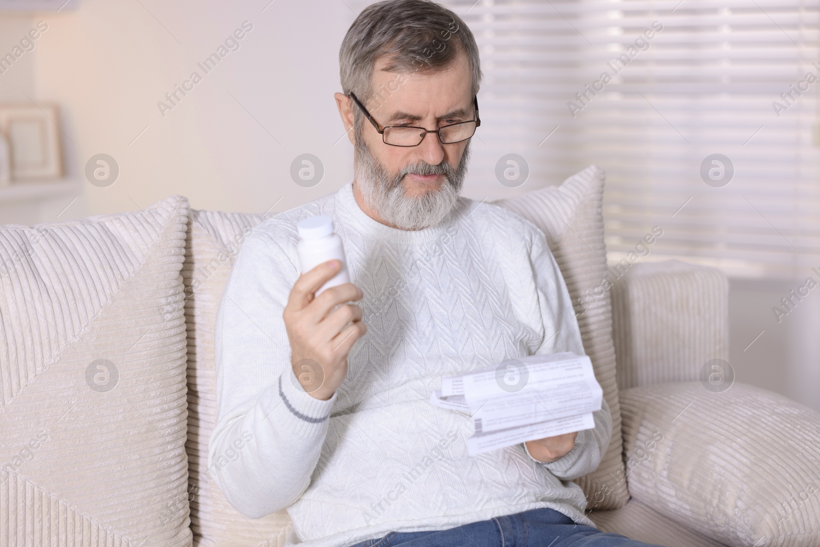 Photo of Senior man with bottle of pills reading instruction indoors