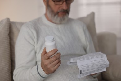 Photo of Senior man with bottle of pills reading instruction indoors, selective focus