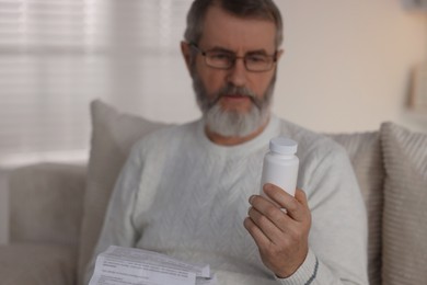 Photo of Senior man with bottle of pills and instruction at home, selective focus