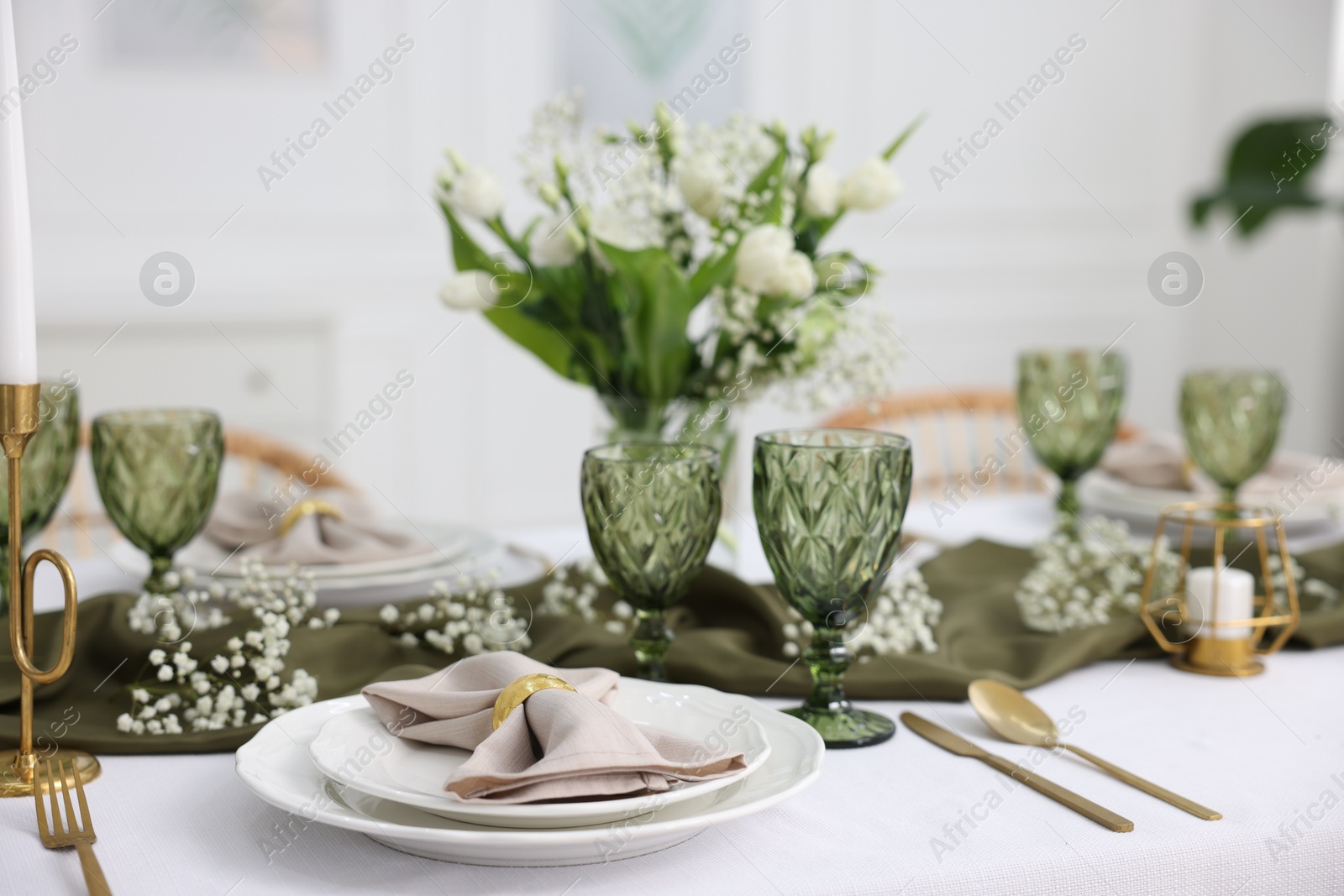 Photo of Color accent table setting with glasses, flowers and green napkins indoors, closeup