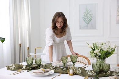 Happy young woman setting table for dinner at home