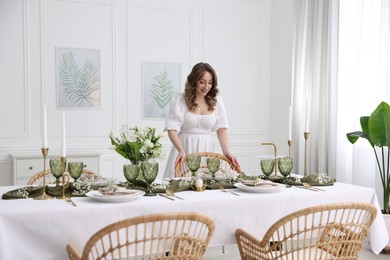 Happy young woman setting table for dinner at home