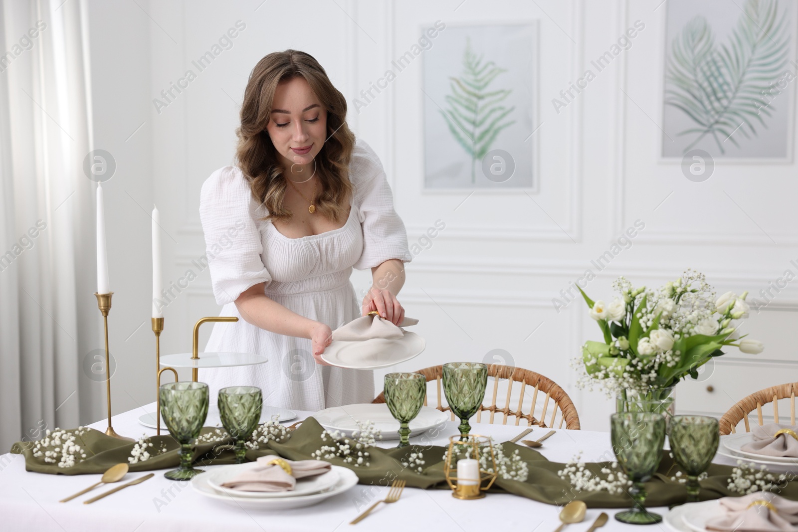 Photo of Young woman setting table for dinner at home