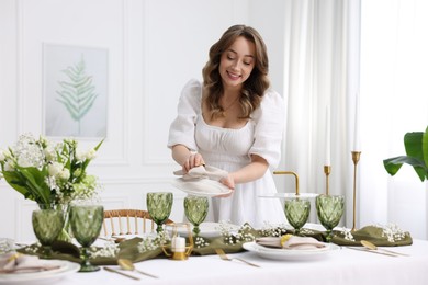 Happy young woman setting table for dinner at home