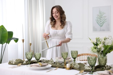 Happy young woman setting table for dinner at home