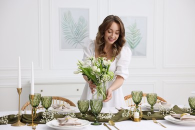 Happy young woman setting table for dinner at home