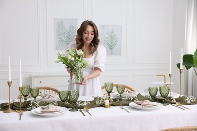 Happy young woman setting table for dinner at home