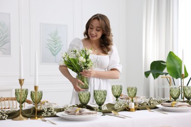 Happy young woman setting table for dinner at home