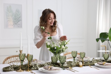 Happy young woman setting table for dinner at home