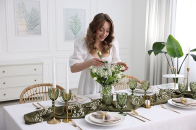 Happy young woman setting table for dinner at home