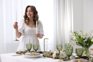 Happy young woman setting table for dinner at home