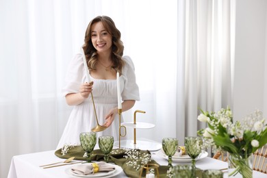 Happy young woman setting table for dinner at home