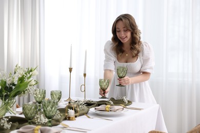 Happy young woman setting table for dinner at home