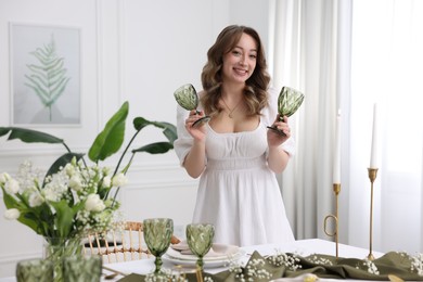 Happy young woman setting table for dinner at home