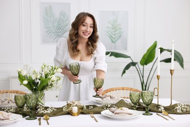 Happy young woman setting table for dinner at home