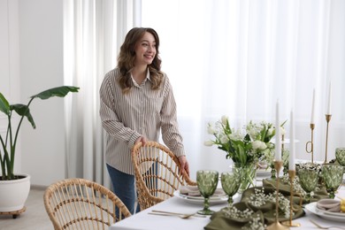 Happy young woman setting table for dinner at home