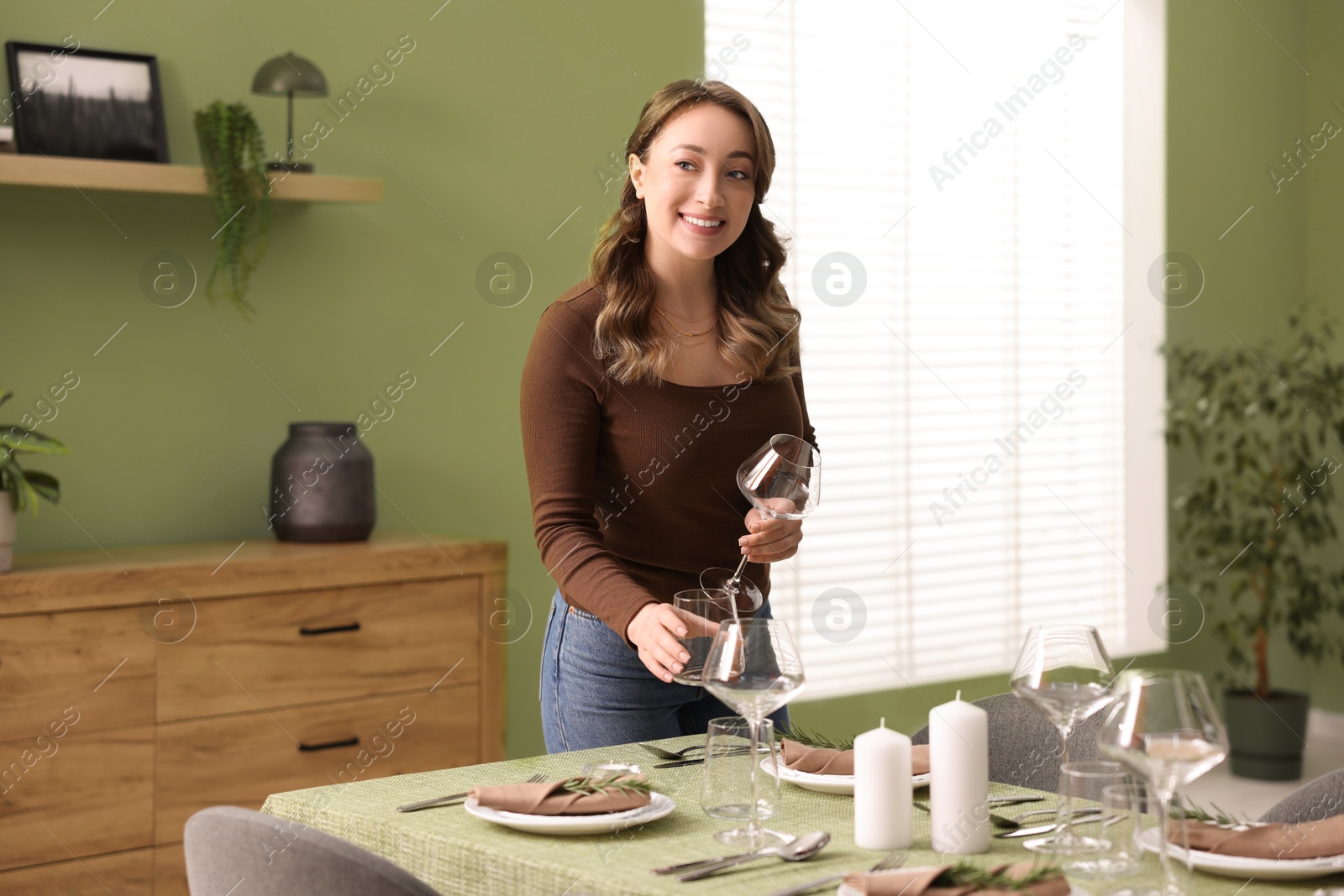 Photo of Happy young woman setting table for dinner at home